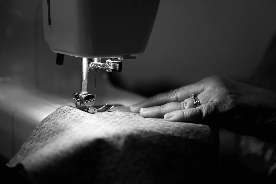 A hand guiding wool cloth under a sewing machine foot