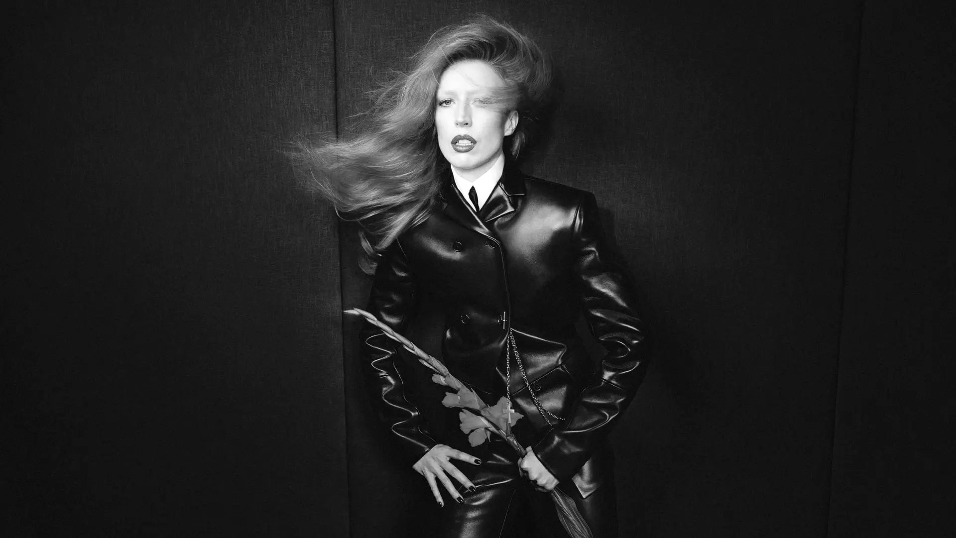 A woman in a long black leather coat against a dark wall