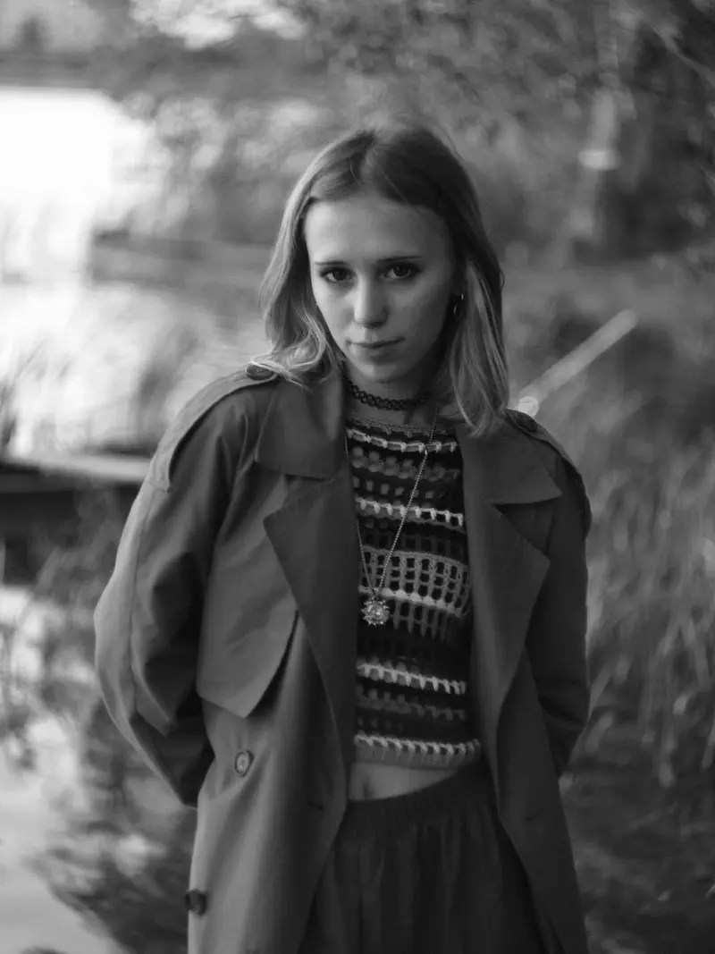 A woman in a trench coat by the water, in black and white