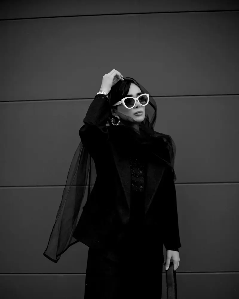 A woman dressed entirely in black against a grey wall